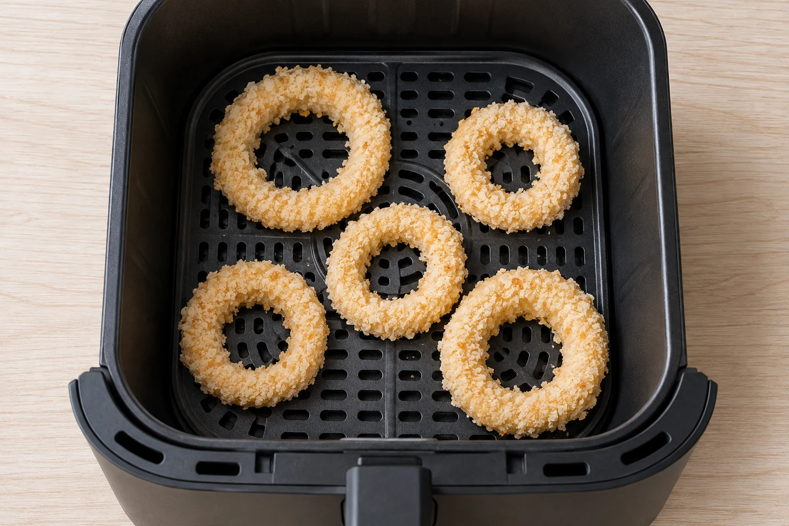 Aros de cebolla con panko colocados en una sola capa sobre la placa perforada de la cesta.